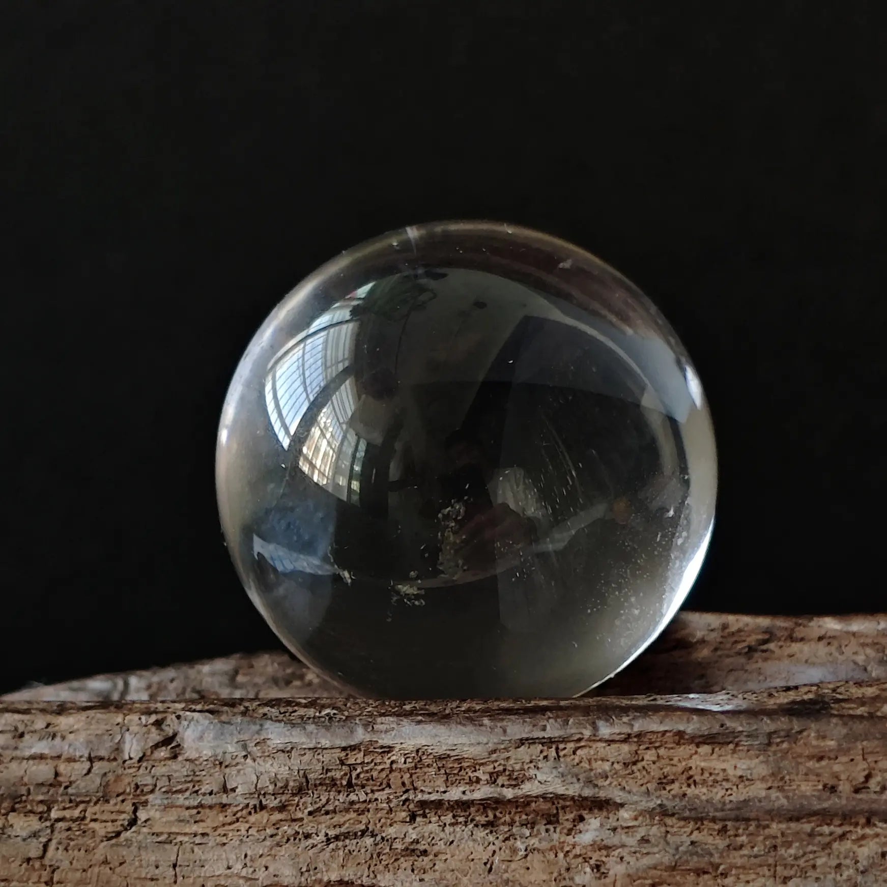 Single high-clarity clear quartz sphere reflecting ambient light, showcasing optical purity; includes small resin display base
