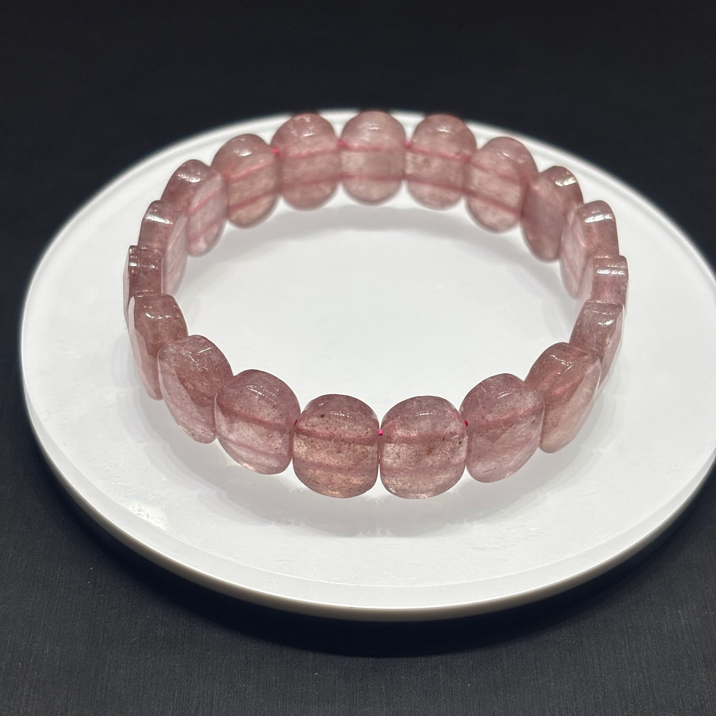 Close-up side view of Strawberry Quartz bracelet on white plate edge, highlighting faceted oval beads and natural inclusions
