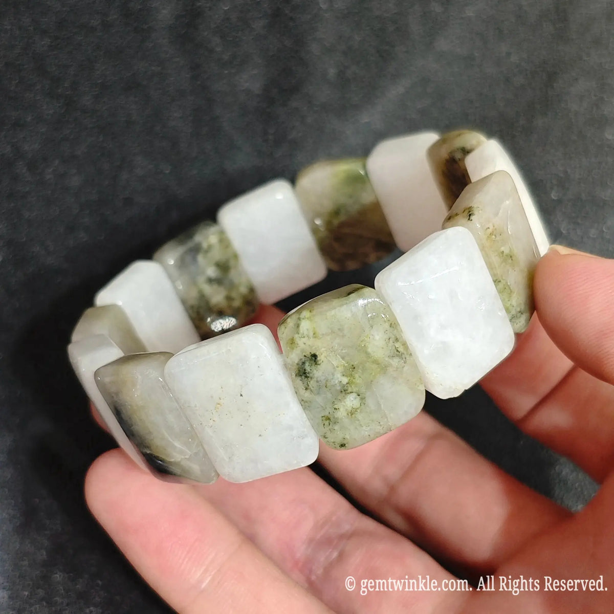 Hand displaying a snowy white golden jadeite quartz smooth segment stretch bracelet highlighting earthy green mineral veins
