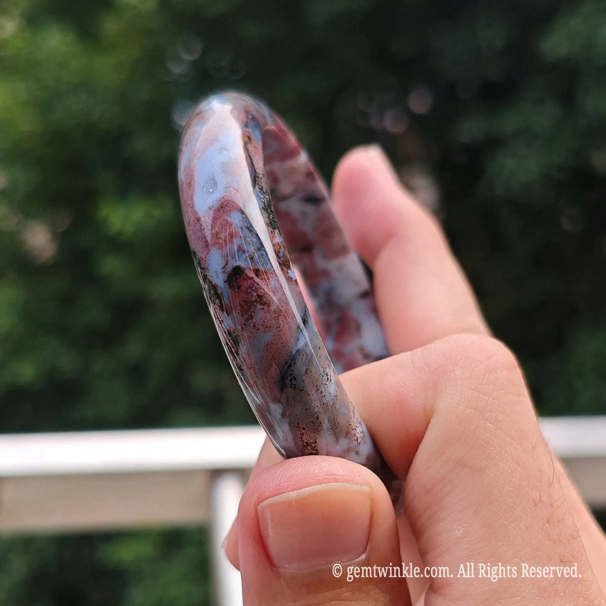 Hand displaying the thickness and polished finish of a natural pink ocean jasper solid stone bangle bracelet