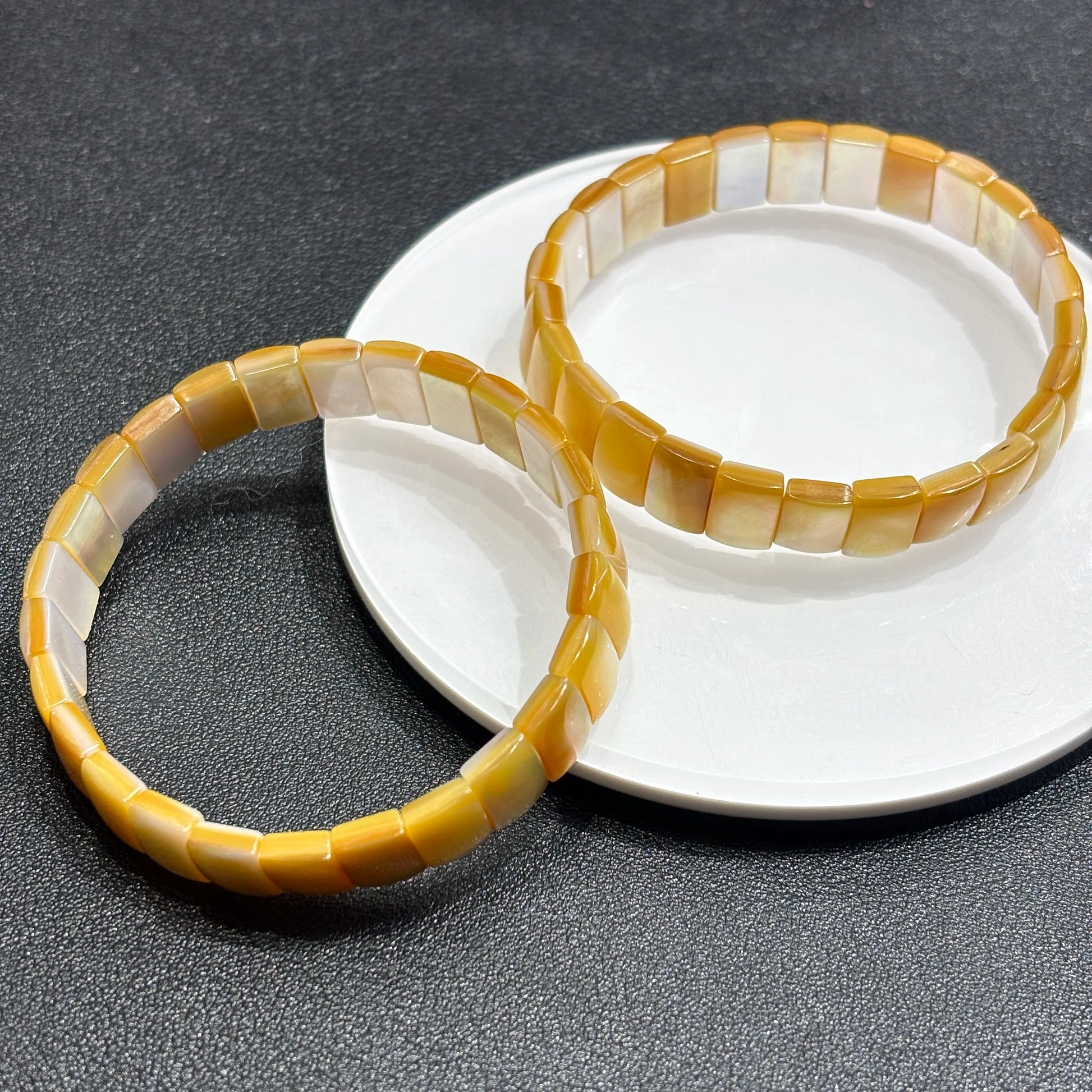Two natural golden shell rectangle bead bangles layered on white dish; highlights organic variation and boho-chic elegance for daily styling