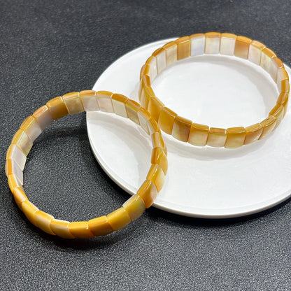 Two natural golden shell rectangle bead bangles layered on white dish; highlights organic variation and boho-chic elegance for daily styling