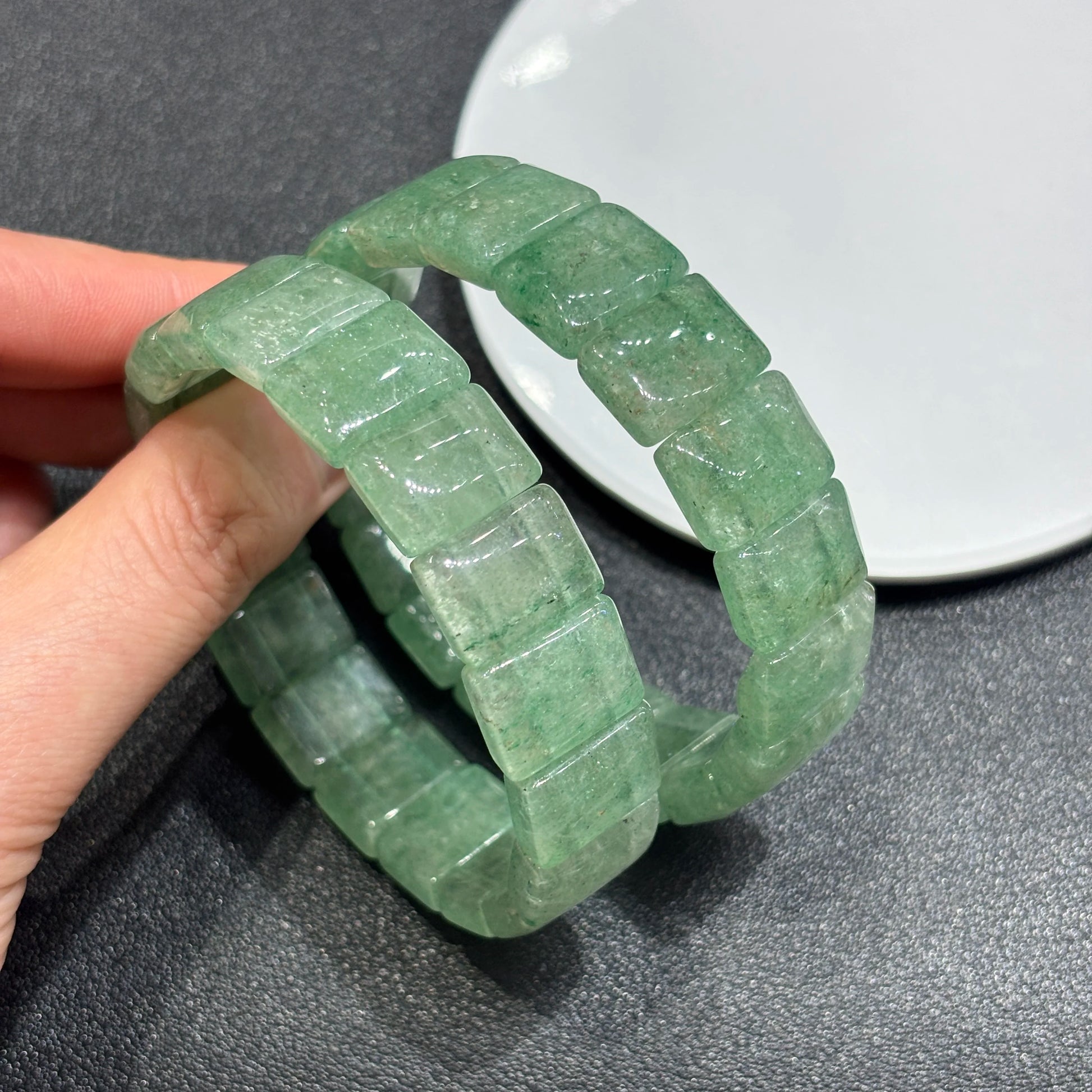 Two natural green strawberry quartz tablet bead bracelets layered on hand; showcases precise square cuts and organic cloud patterns