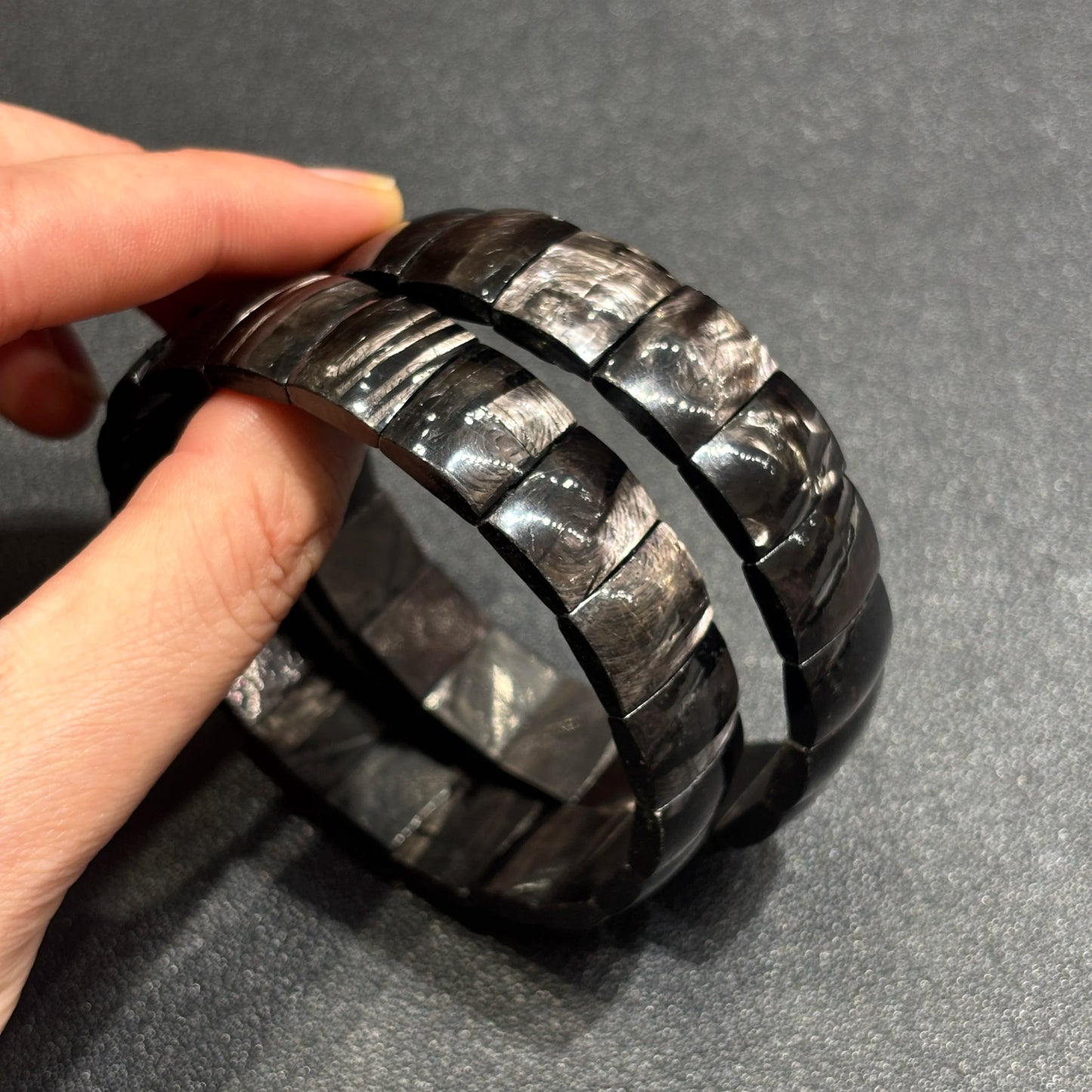 Two natural hypersthene faceted tablet bead bracelets held in hand; showcases layered depth and metallic luster under studio light