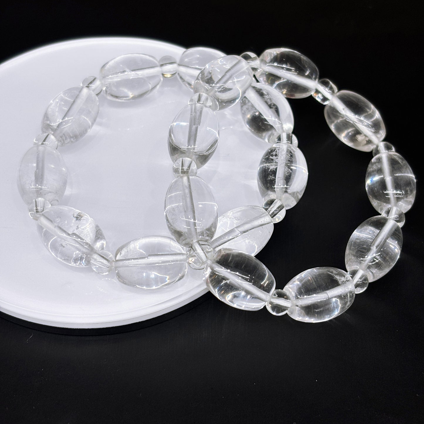 Two clear quartz oval drum bead bracelets layered on white disc, modern stacking jewelry idea
