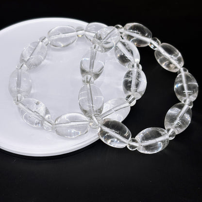Two clear quartz oval drum bead bracelets layered on white disc, modern stacking jewelry idea