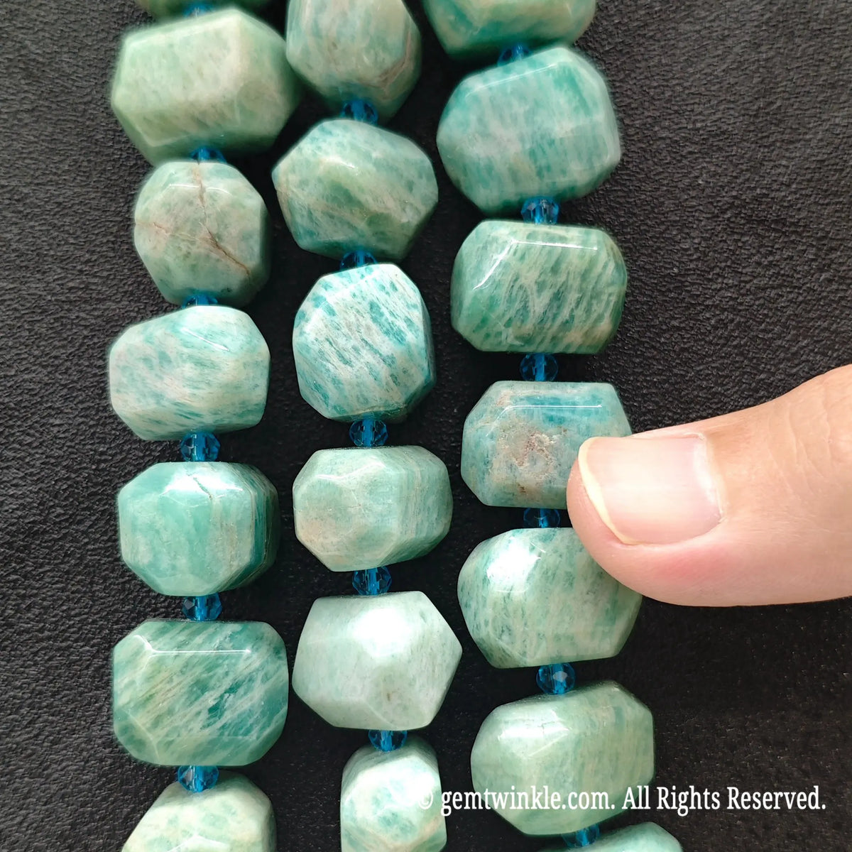 Hand holding three strands of natural green amazonite freeform faceted gemstone beads showing white feldspar striations