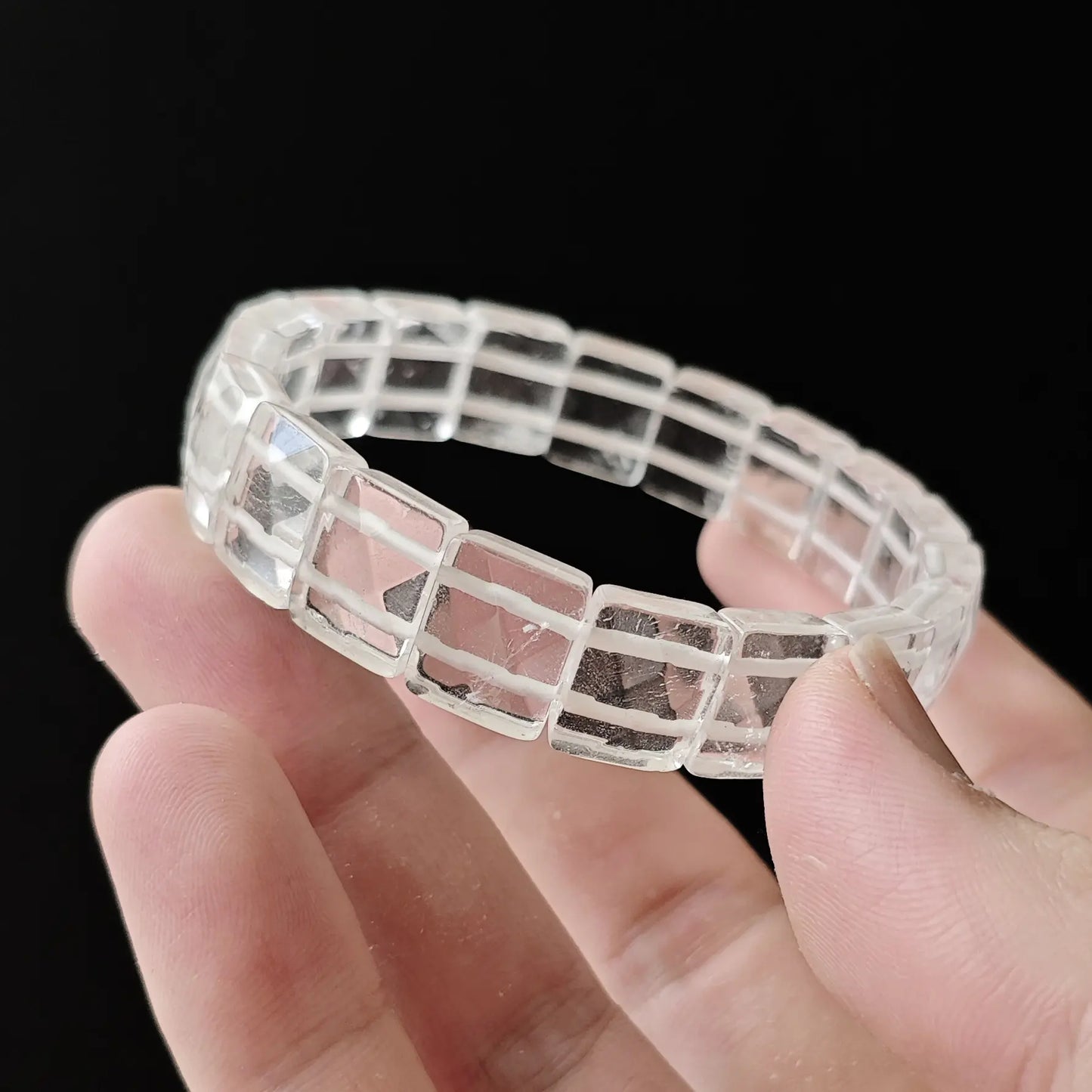 Faceted quartz beads stretched between fingers—secure knotting, elastic resilience, uniform alignment of cut faces