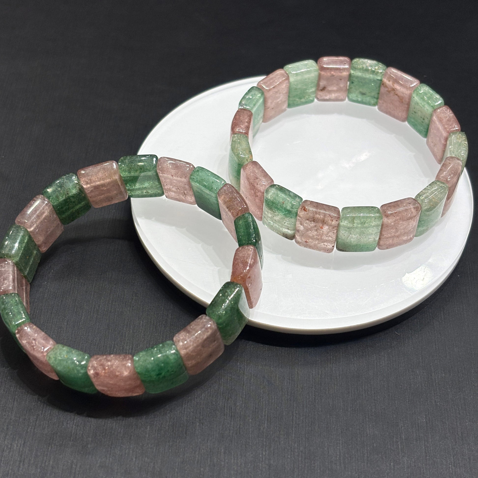 Matching pink and green strawberry quartz slab bracelets arranged artistically on dark surface, minimalist jewelry design