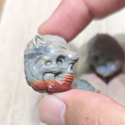 A close-up of a hand holding a small carved gray cat figurine with a red-orange painted section near the base, against a light neutral background.