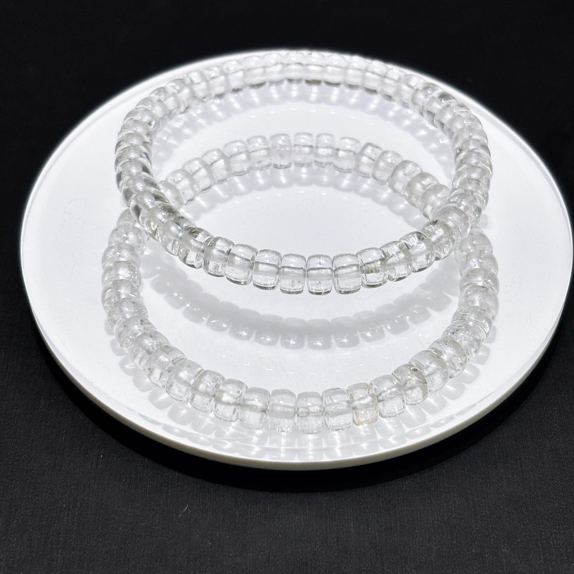 Double stack of transparent quartz disc bead bracelets on white plate, boho aesthetic