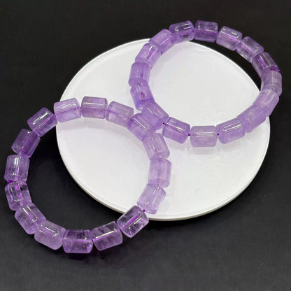 Two matching light purple amethyst crystal bracelets arranged overlapping on a white ceramic dish, highlighting their uniform bead shape and gentle lavender hue.