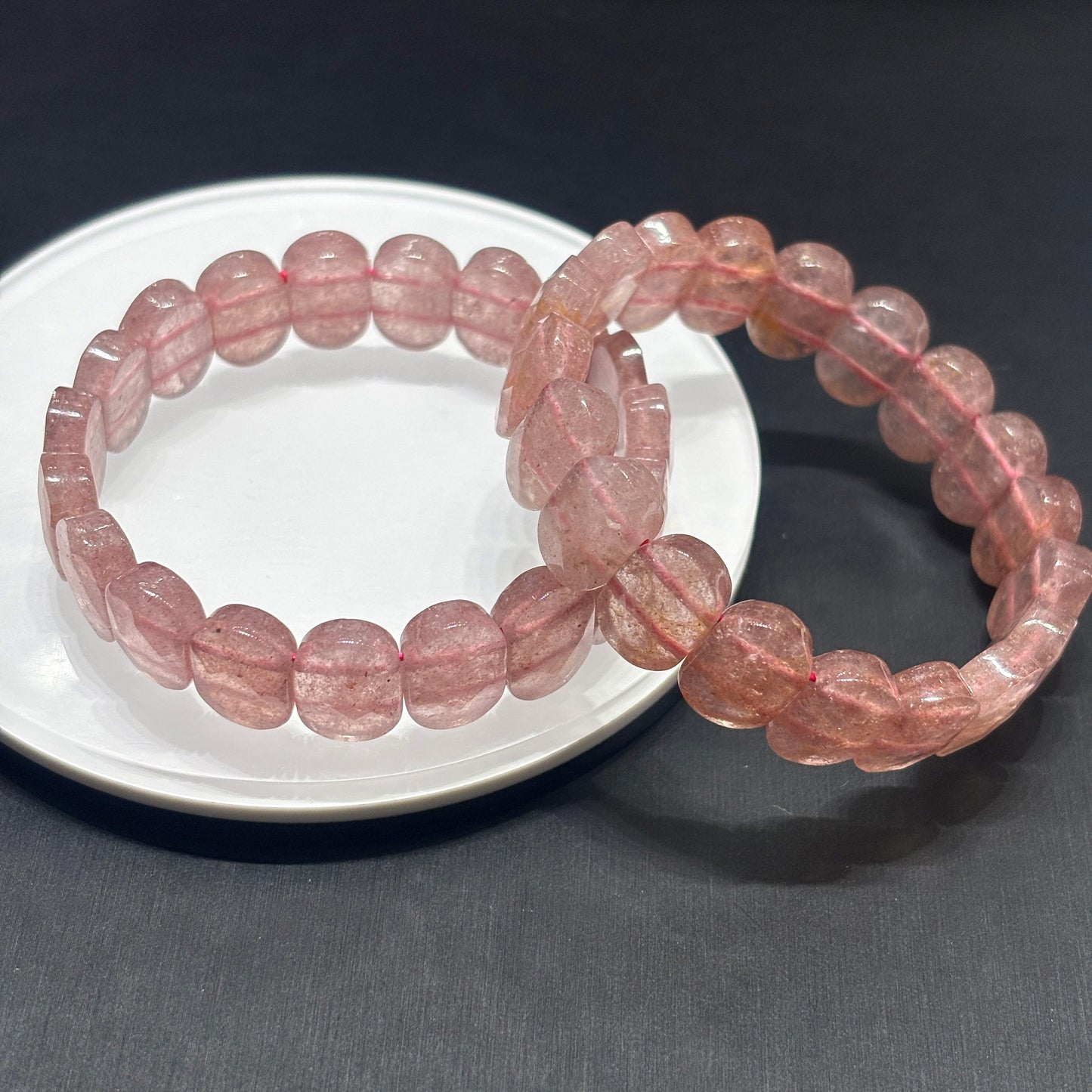Two natural Strawberry Quartz bracelets arranged on white ceramic plate, pink oval beads, chakra healing jewelry for women