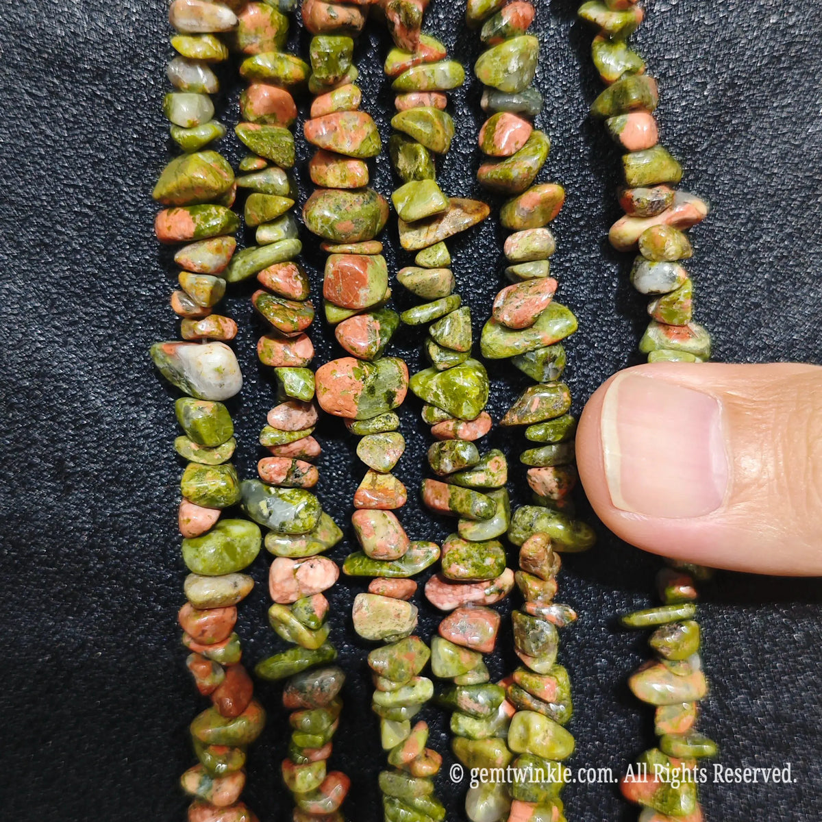 Close up hand holding natural unakite stone chips displaying polished green and pink surfaces with fine drill holes