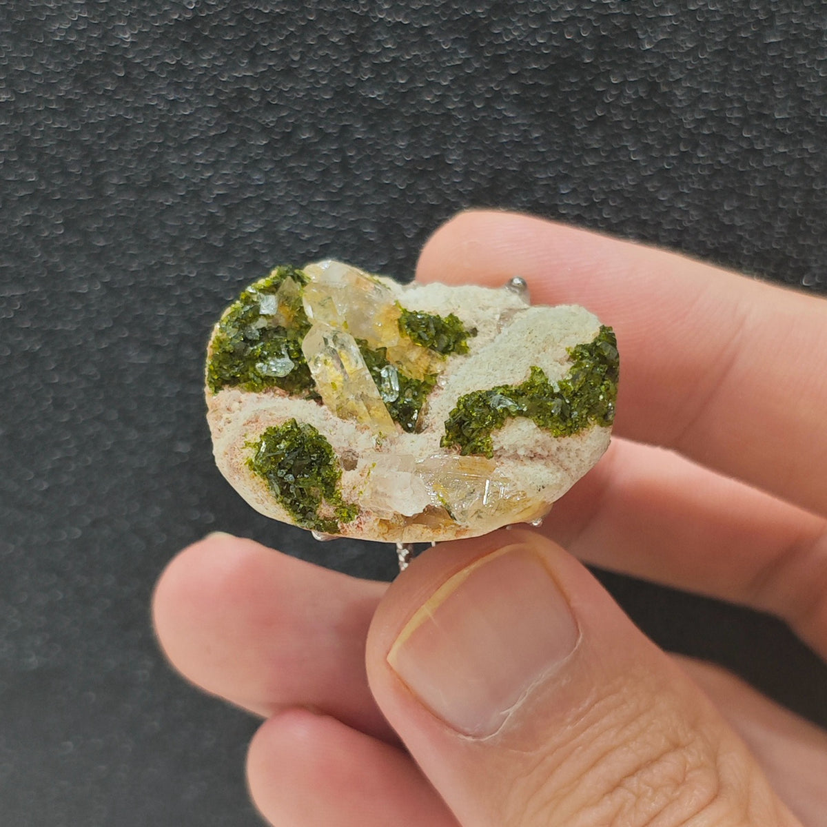 uncut raw epidote mineral slice ring held under studio light
