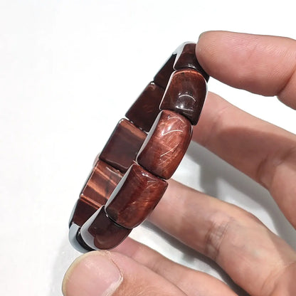 Wrist shot of a unisex red tiger eye bracelet with rectangular beads (~16mm long). Deep reddish-brown base with golden-orange chatoyant bands on an 18cm elastic strand.