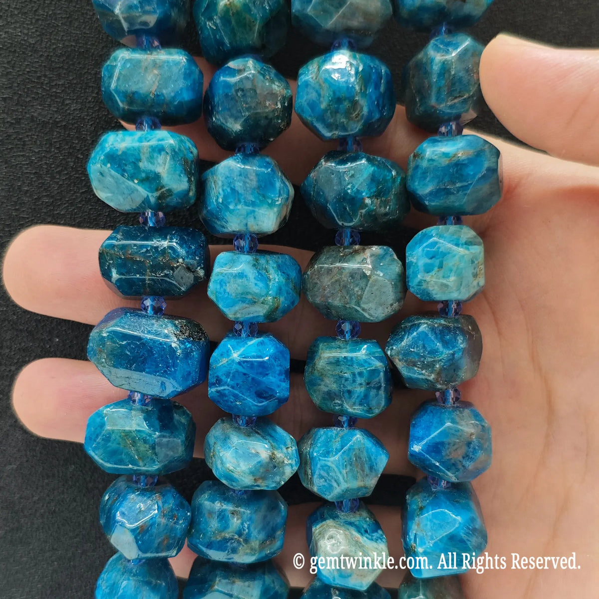 Hand holding three strands of natural blue apatite faceted freeform beads showing rich ocean blue crystal clarity