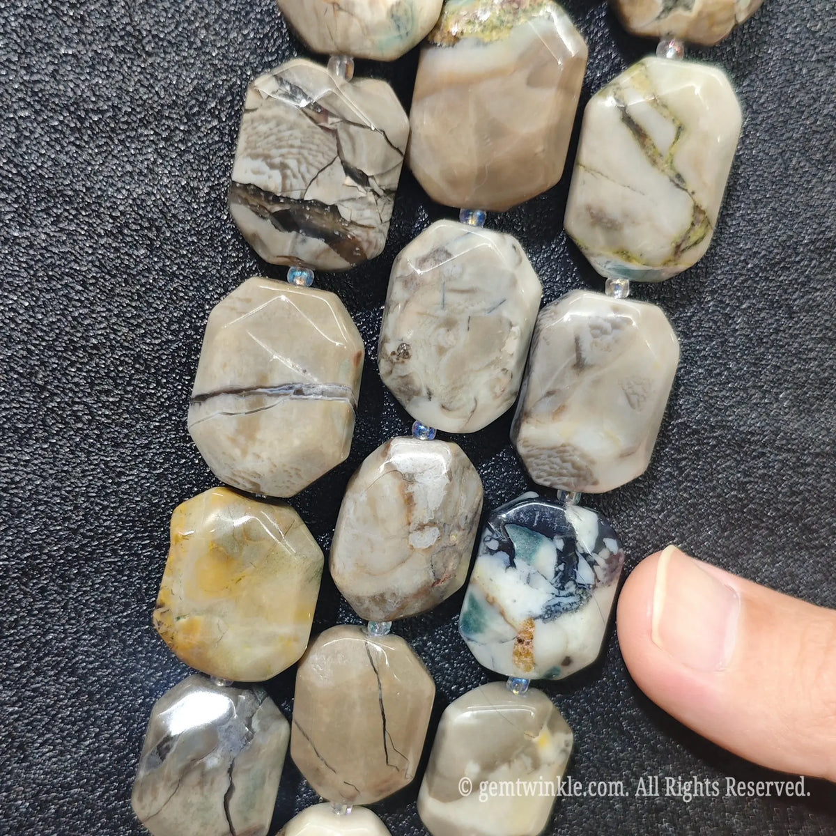 Hand holding four strands of natural volcanic ash agate faceted flat slab beads showing earthy grey tones