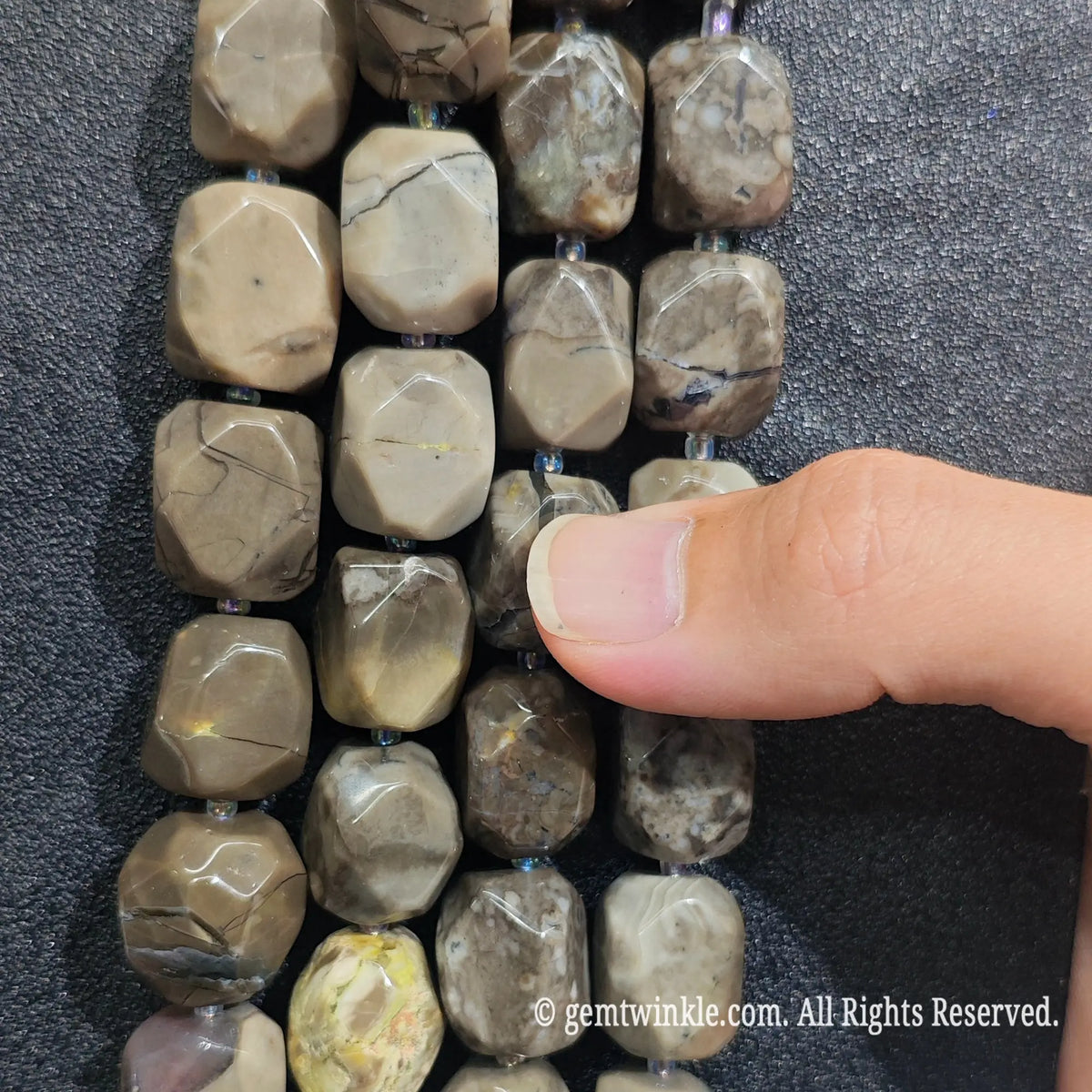 Hand inspecting volcanic ash agate freeform beads displaying organic faceted surfaces and natural stone texture