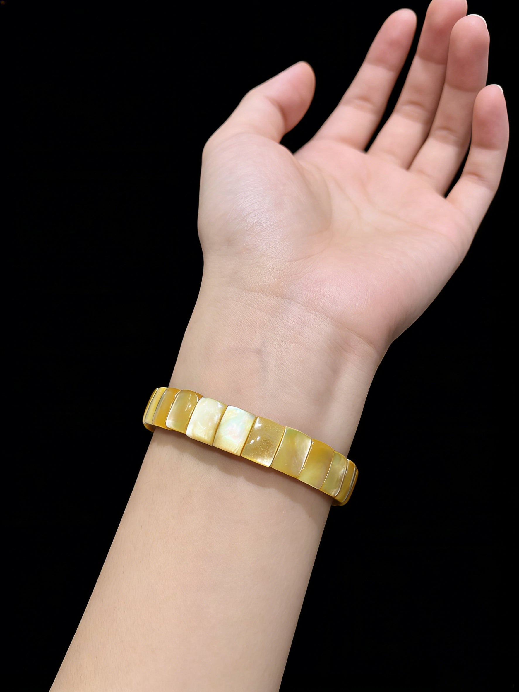 Hand wearing natural golden shell rectangle bead bangle; soft luster complements skin tone, ideal as a dainty girl gift or travel memento