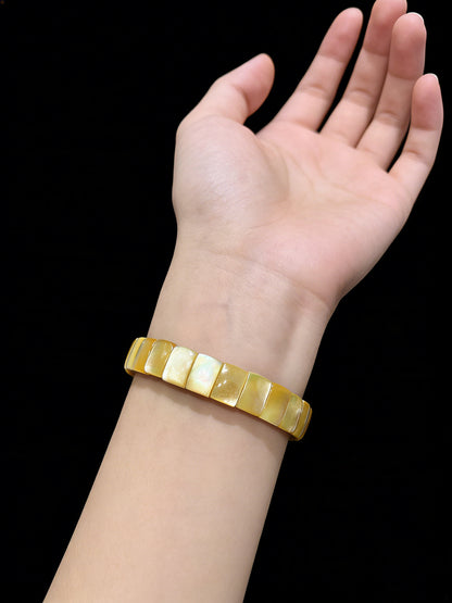 Hand wearing natural golden shell rectangle bead bangle; soft luster complements skin tone, ideal as a dainty girl gift or travel memento