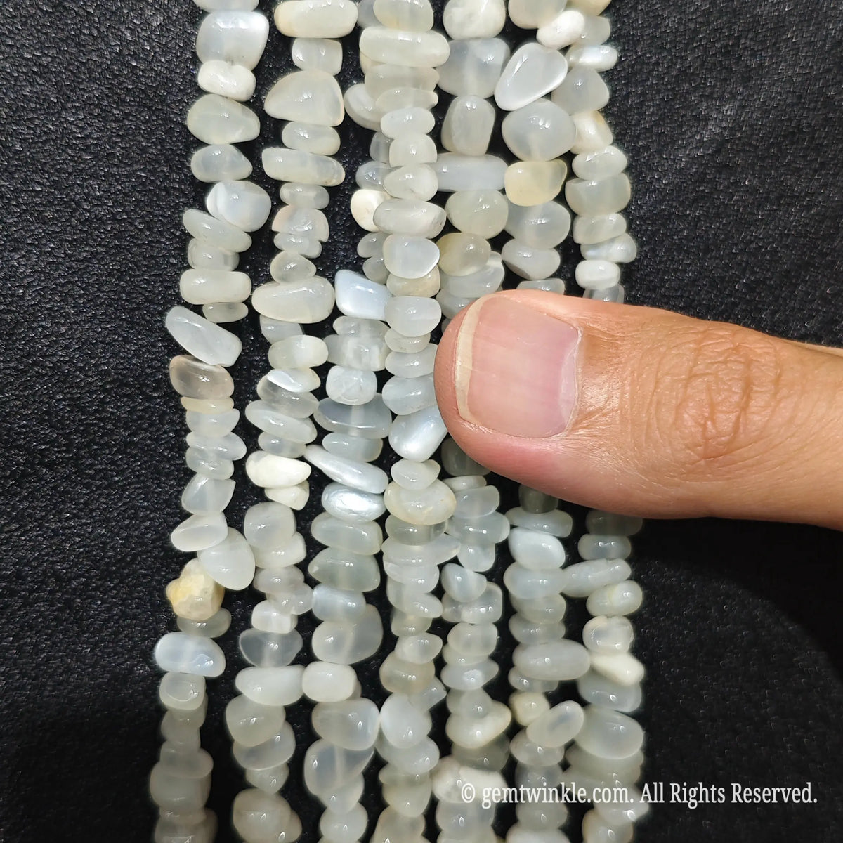 Close up hand holding natural white moonstone stone chips displaying adularescence and fine drill holes[cite: 7]