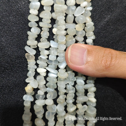 Close up hand holding natural white moonstone stone chips displaying adularescence and fine drill holes[cite: 7]