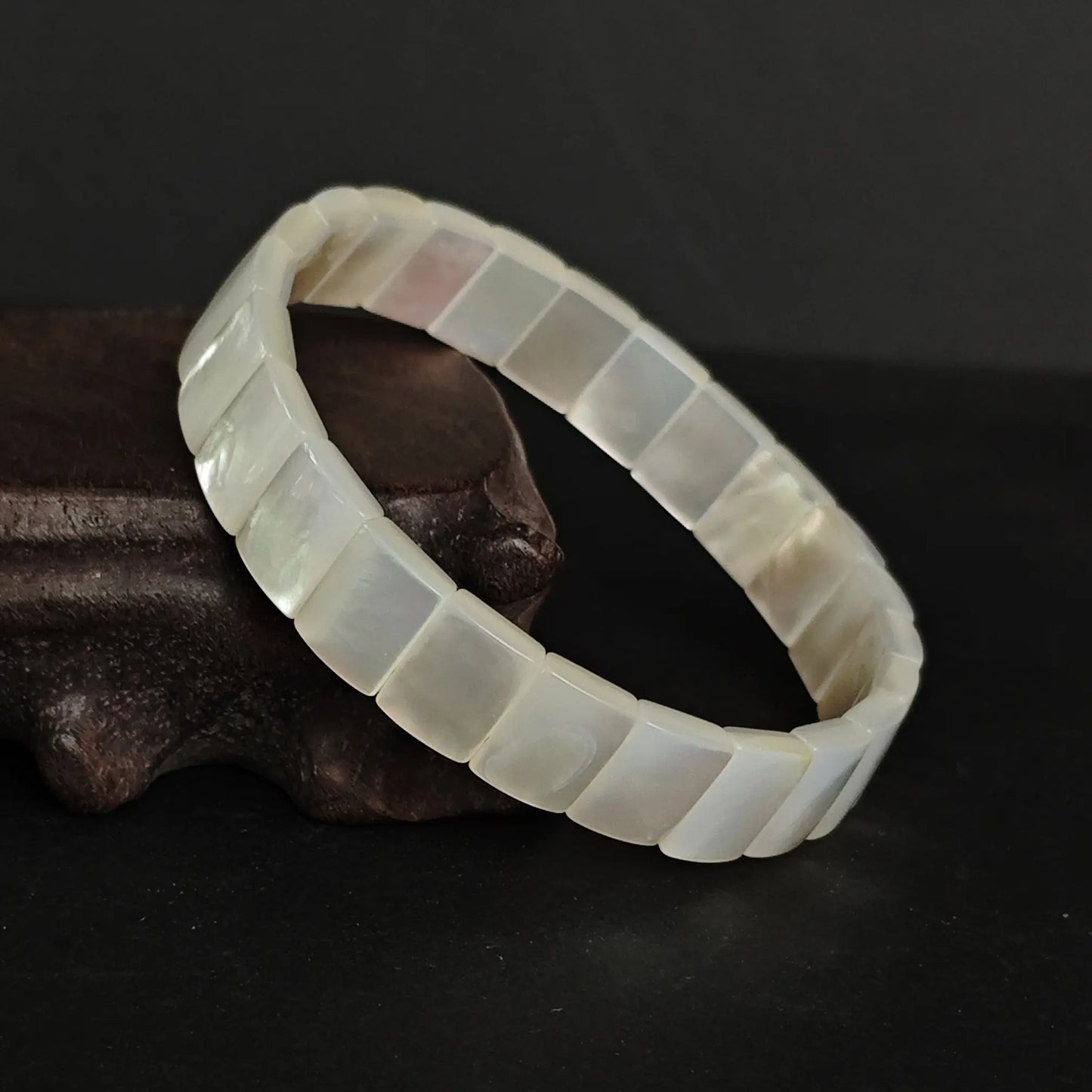 White mother-of-pearl rigid bracelet resting on natural driftwood, emphasizing organic texture and serene aesthetic