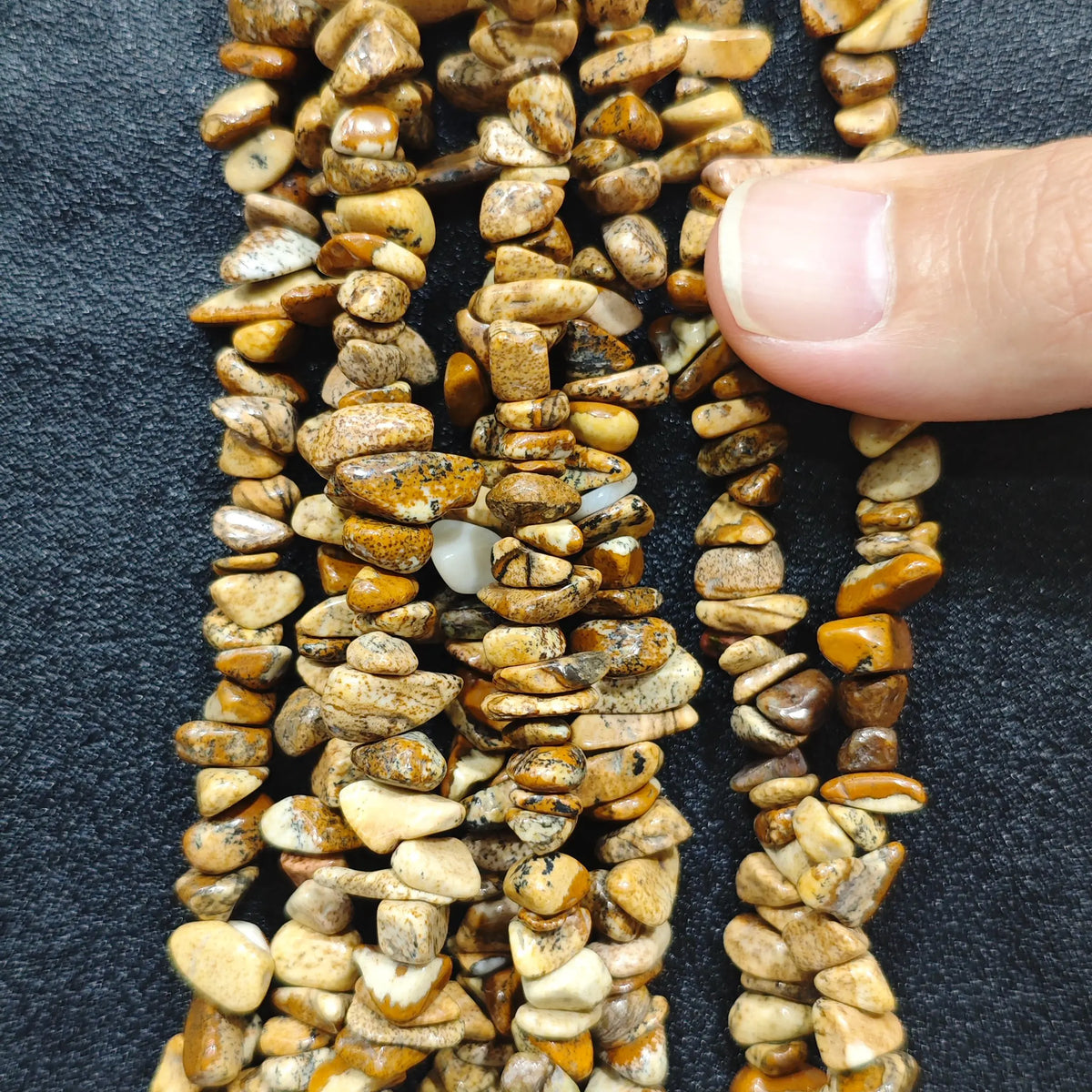 Fingers holding natural wood grain stone gemstone chip beads on black background