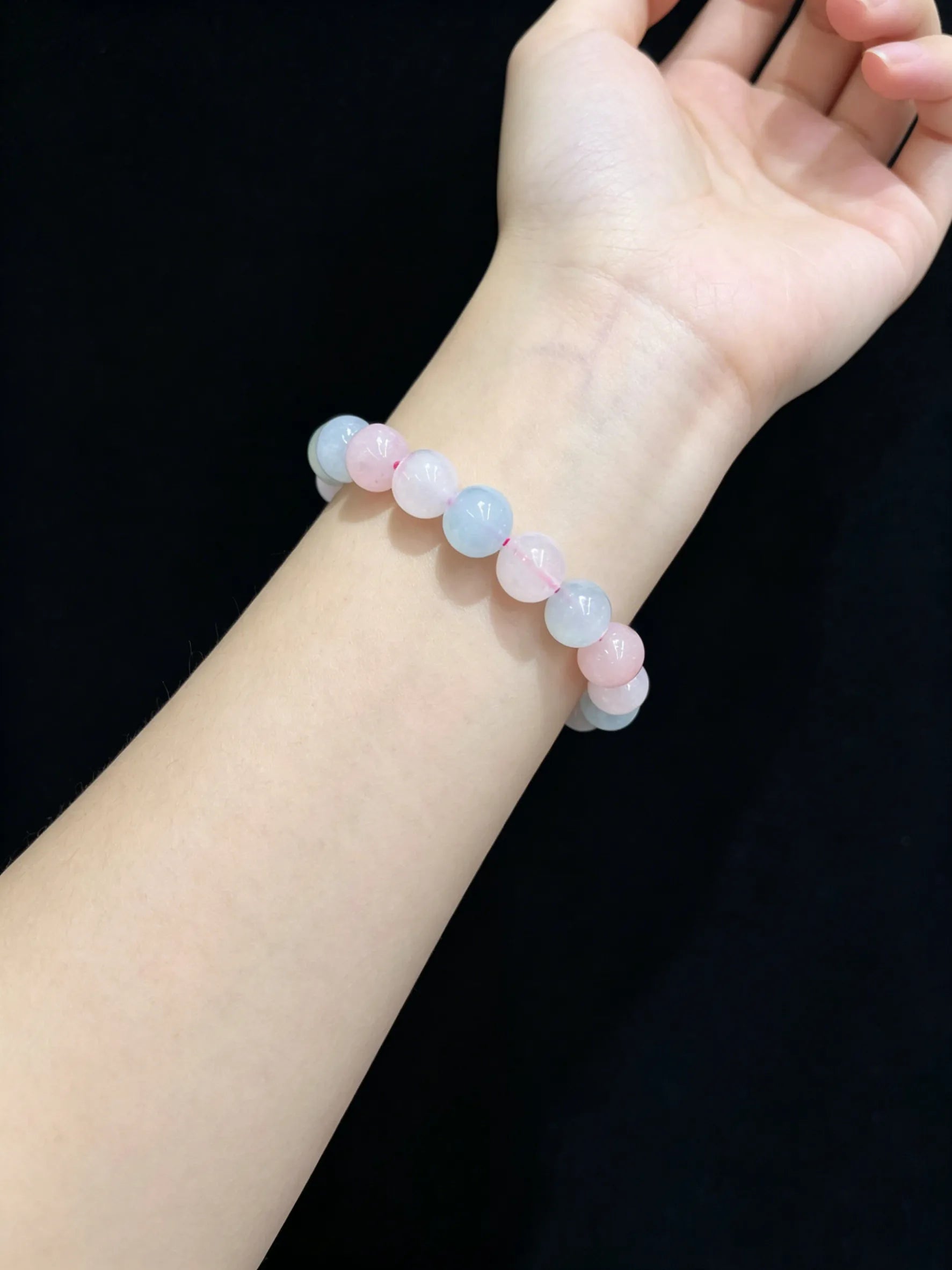 Woman’s wrist wearing natural morganite stretch bracelet, smooth 10mm round beads, soft pastel colors against dark sleeve.