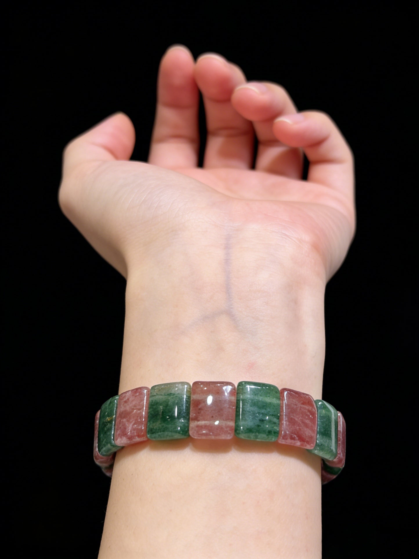 Woman wearing pink and green strawberry quartz slab bracelet on wrist, black background, elegant everyday accessory