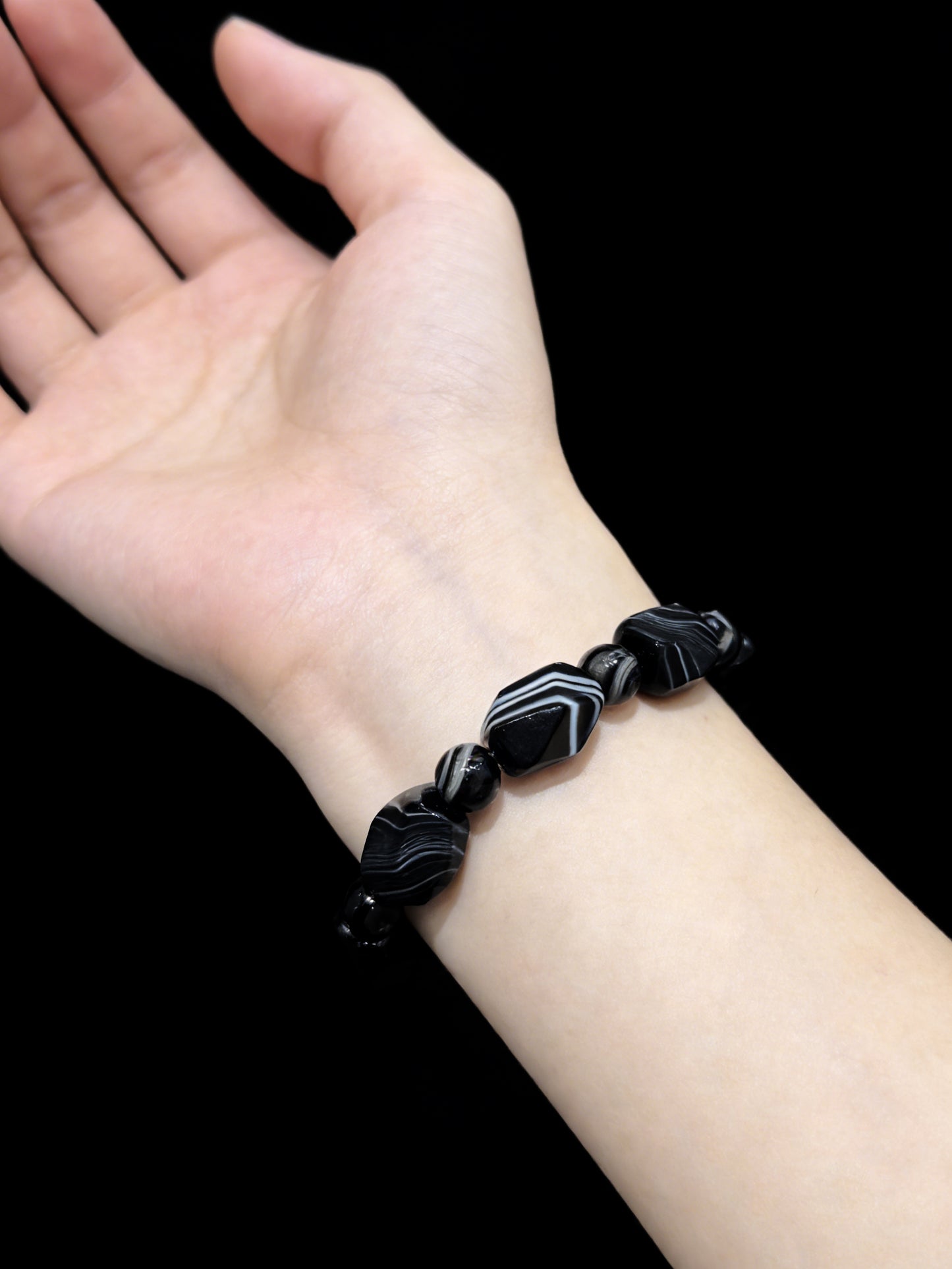 Woman wearing black and white banded agate irregular bead bracelet, modern aesthetic jewelry against black background