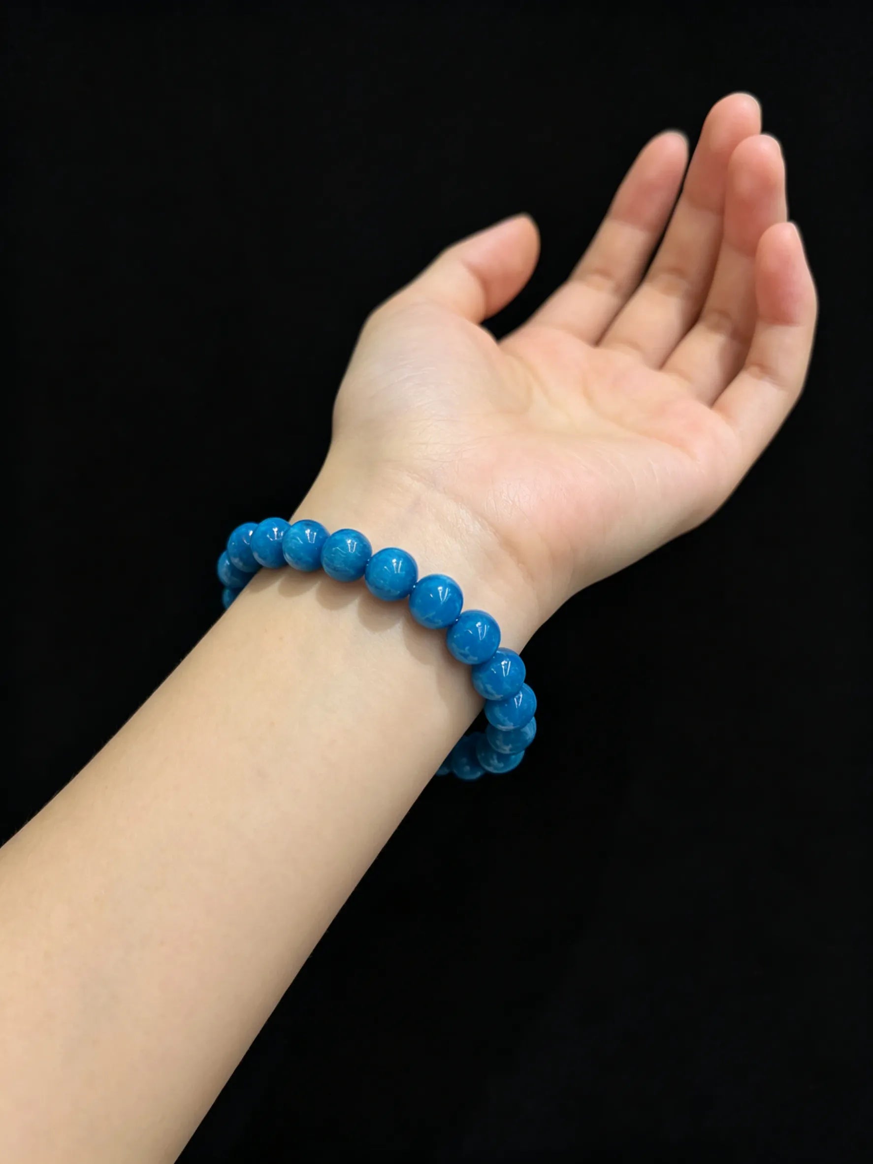 Woman wearing natural blue apatite stretch bracelet on wrist against black background, 9mm beads visible, seamless elastic closure