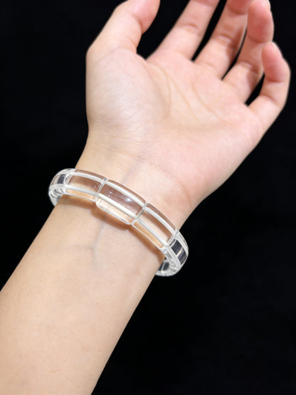Woman wearing clear quartz square tablet bracelet, transparent stackable jewelry against black background