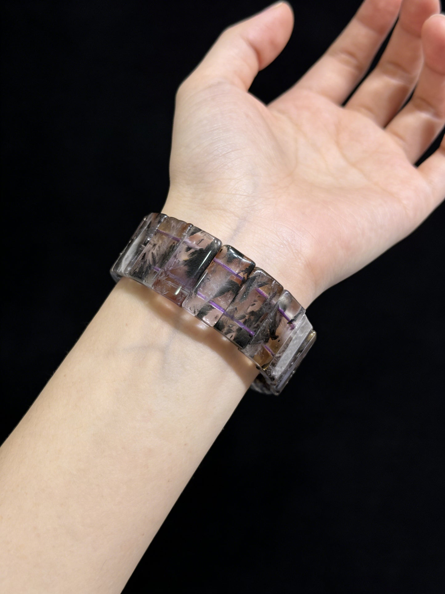 Woman wearing black dream phantom quartz rectangular slab bracelet, elegant dark crystal jewelry against black background