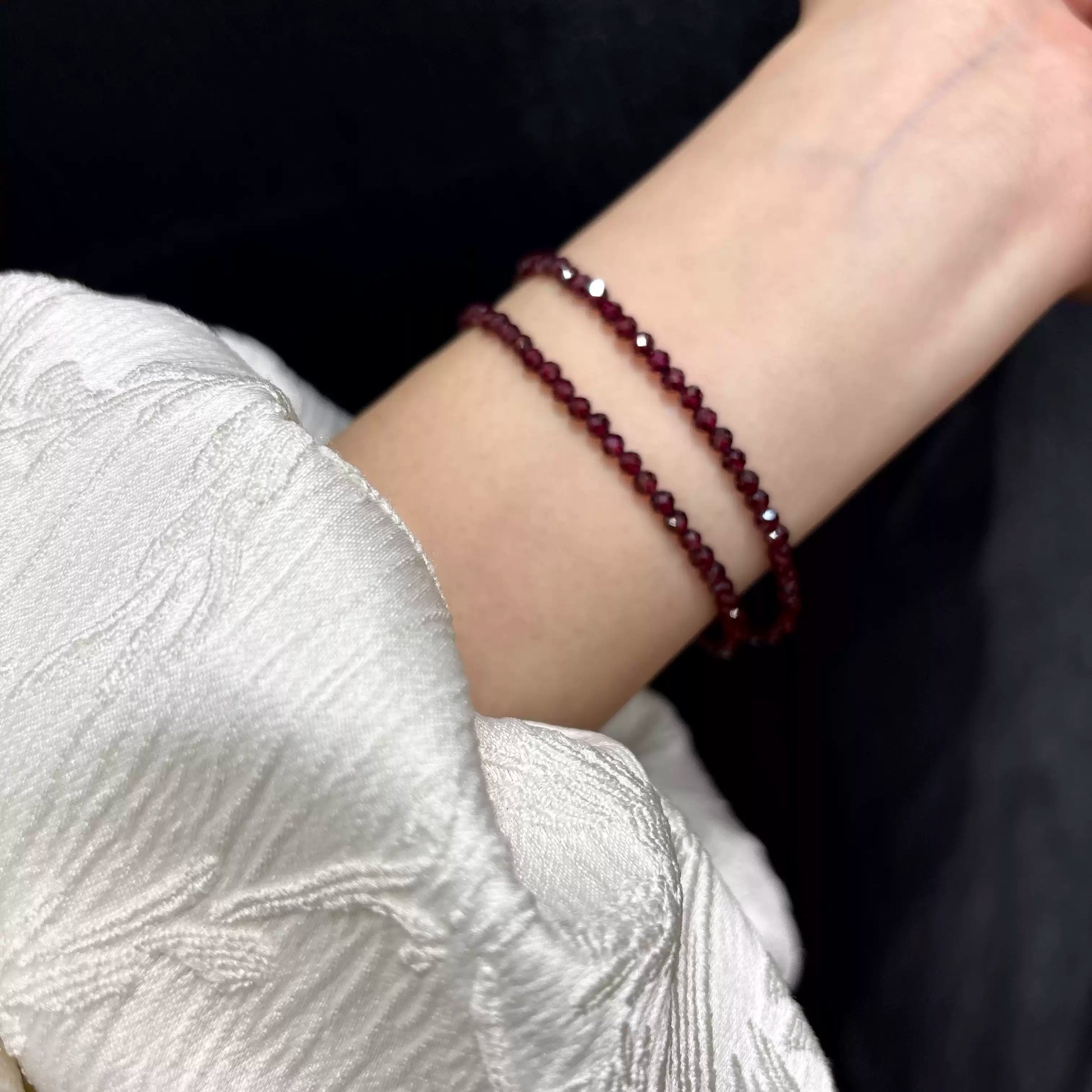 Woman wearing natural garnet dual-wrap bracelet on wrist, two layers of faceted red beads against black background