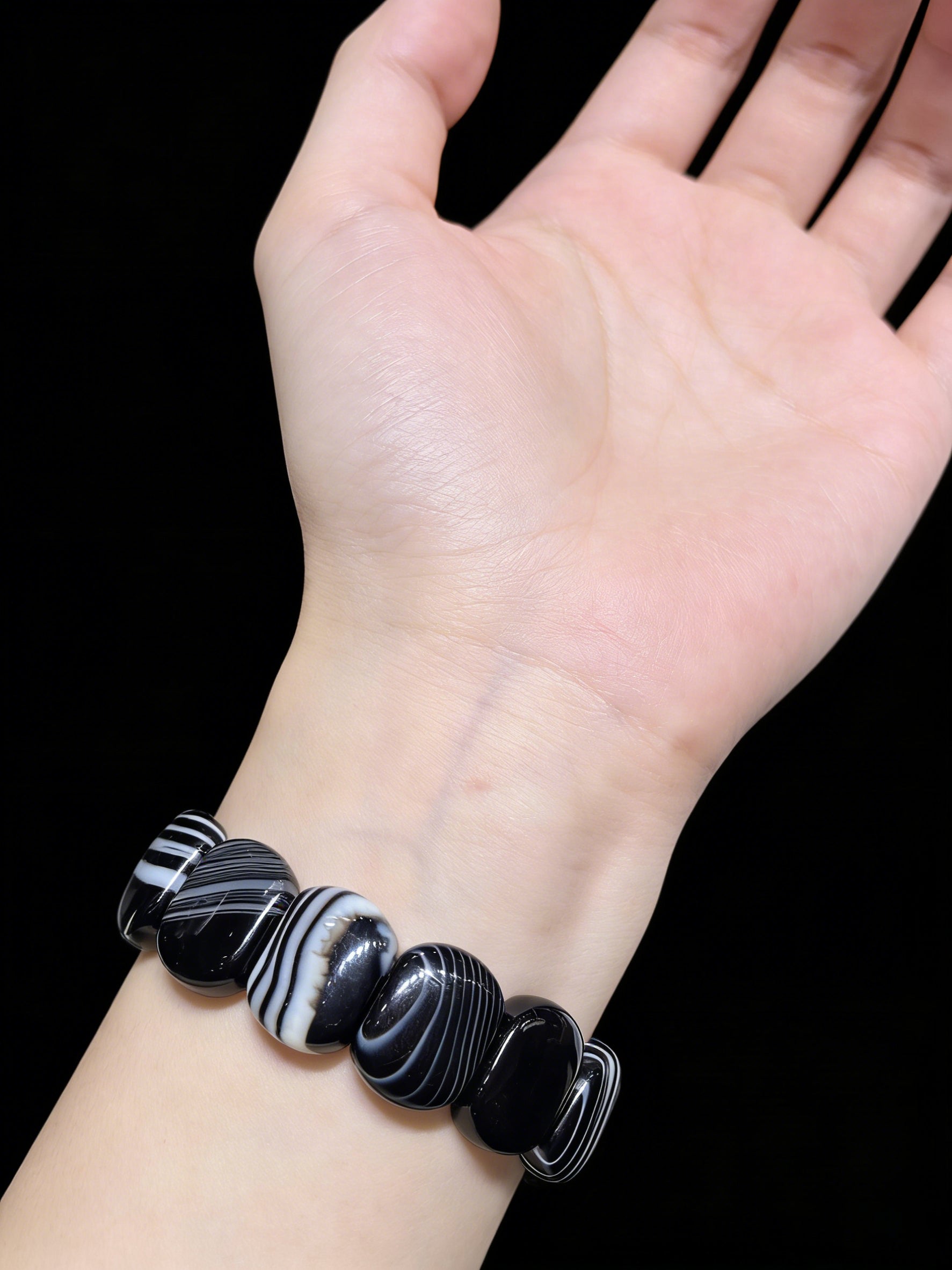 Woman wearing black and white banded onyx square bead bracelet, sleek minimalist jewelry against dark background