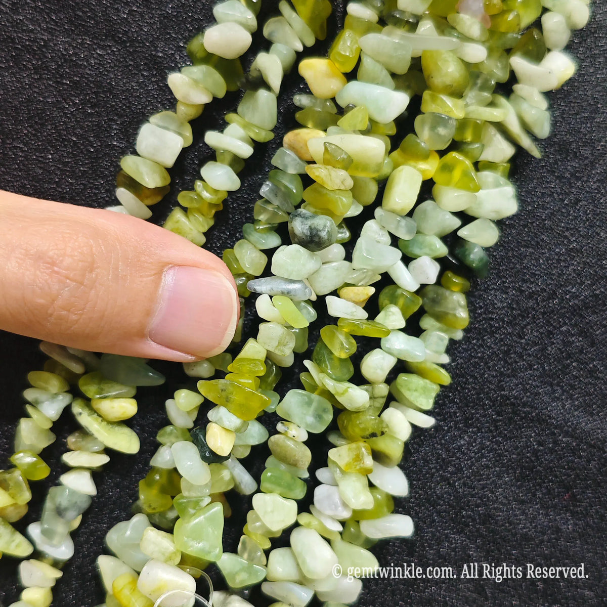Close up hand holding natural serpentine jade stone chips displaying polished surfaces and fine drill holes
