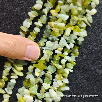 Close up hand holding natural serpentine jade stone chips displaying polished surfaces and fine drill holes
