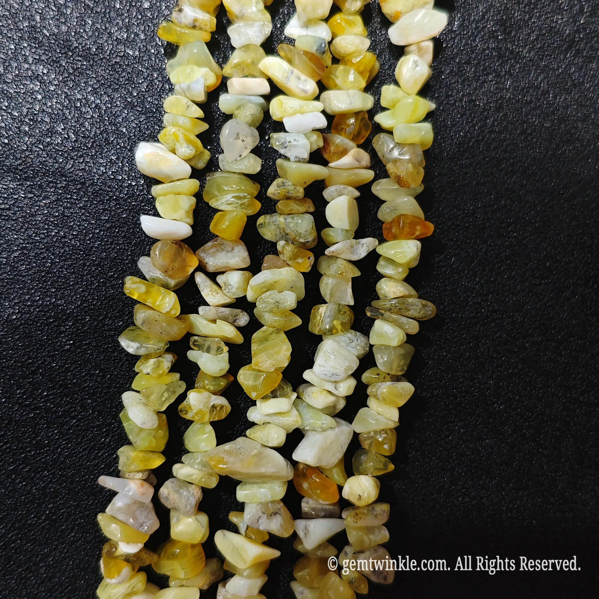 Close up hand holding natural yellow opal stone chips displaying polished surfaces and fine drill holes