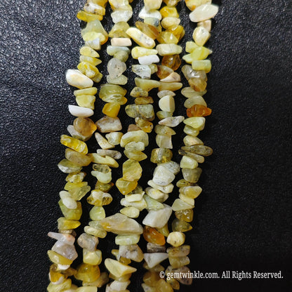 Close up hand holding natural yellow opal stone chips displaying polished surfaces and fine drill holes