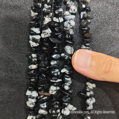 Close up hand holding natural zebra jasper stone chips displaying polished contrast surfaces and fine drill holes[cite: 9]