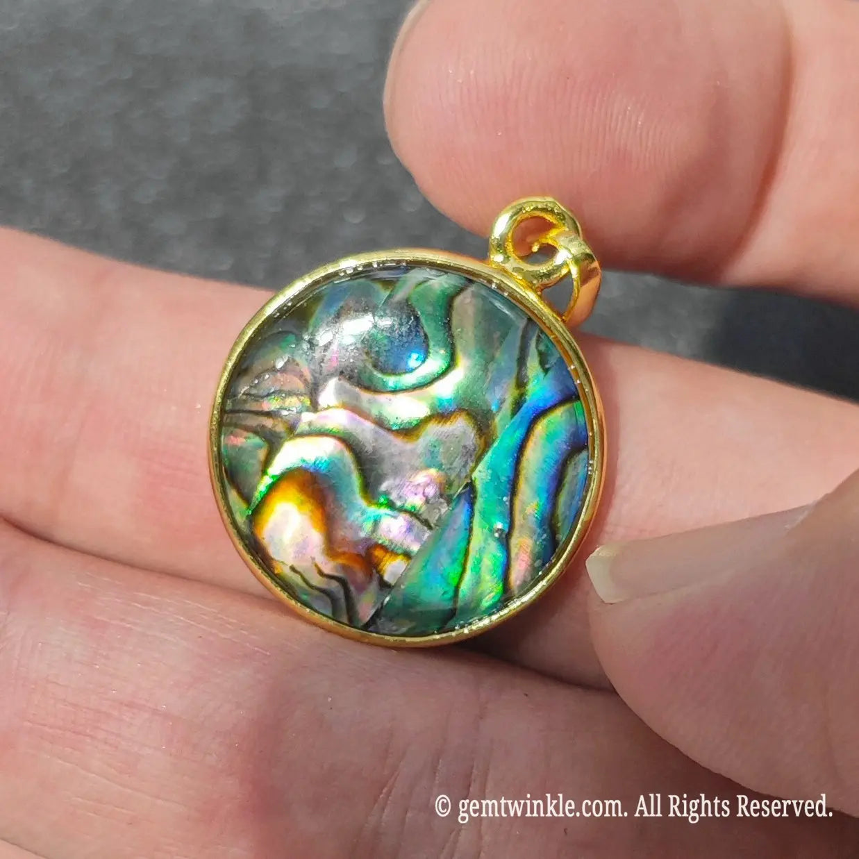 Side angle display of 2cm round abalone shell pendant held in hand showing smooth alloy bezel polish and bail loop