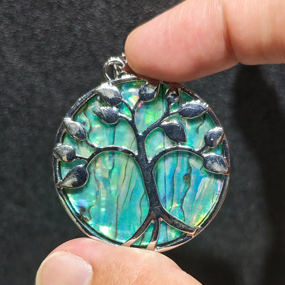 Side angle display of Tree of Life abalone shell pendant held in fingers showcasing smooth alloy rim finish