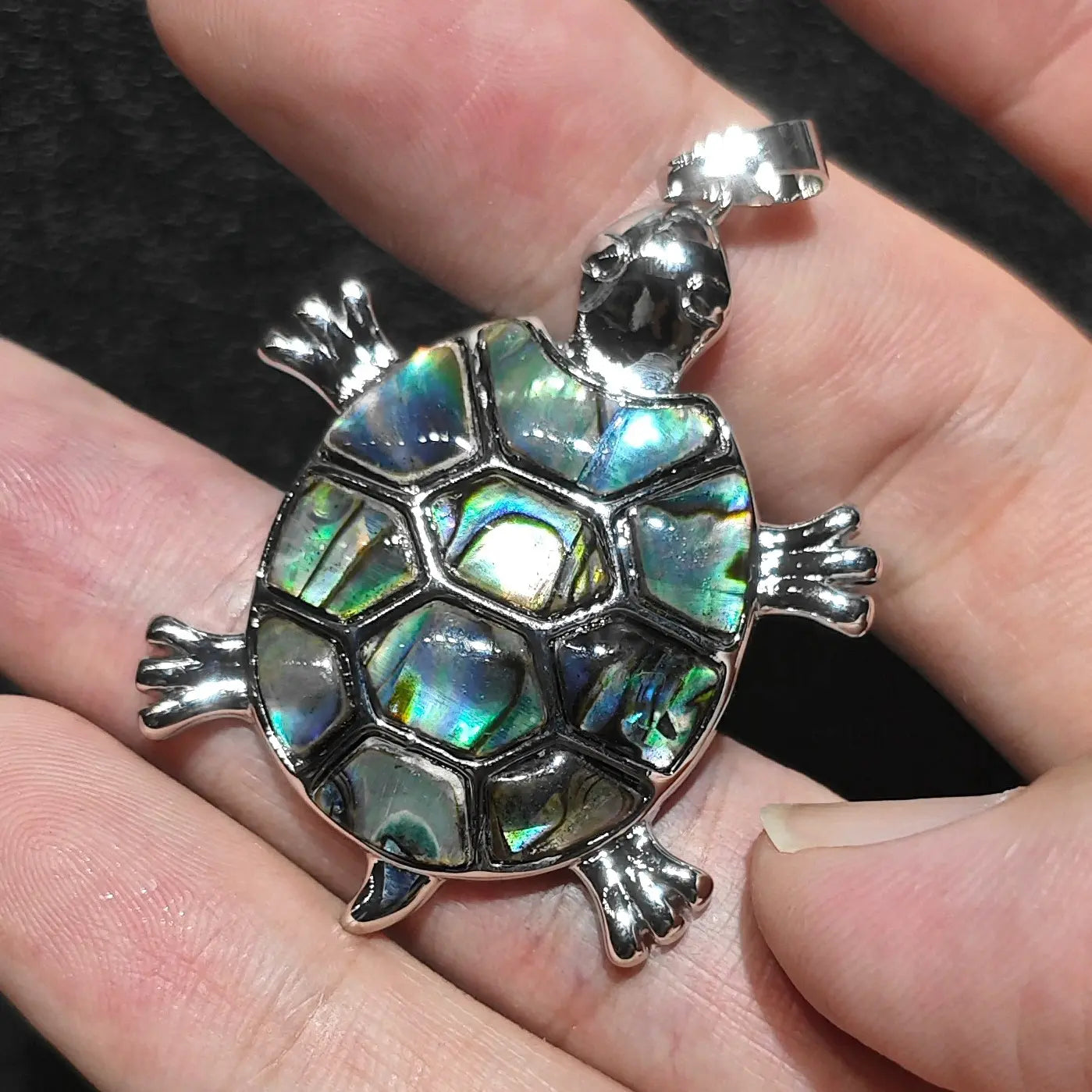 Natural abalone shell sea turtle pendant held in fingers showcasing 35mm size reference against dark background