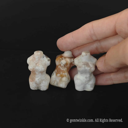 A human hand touching three upright flower agate goddess sculptures to demonstrate the small pocket size scale