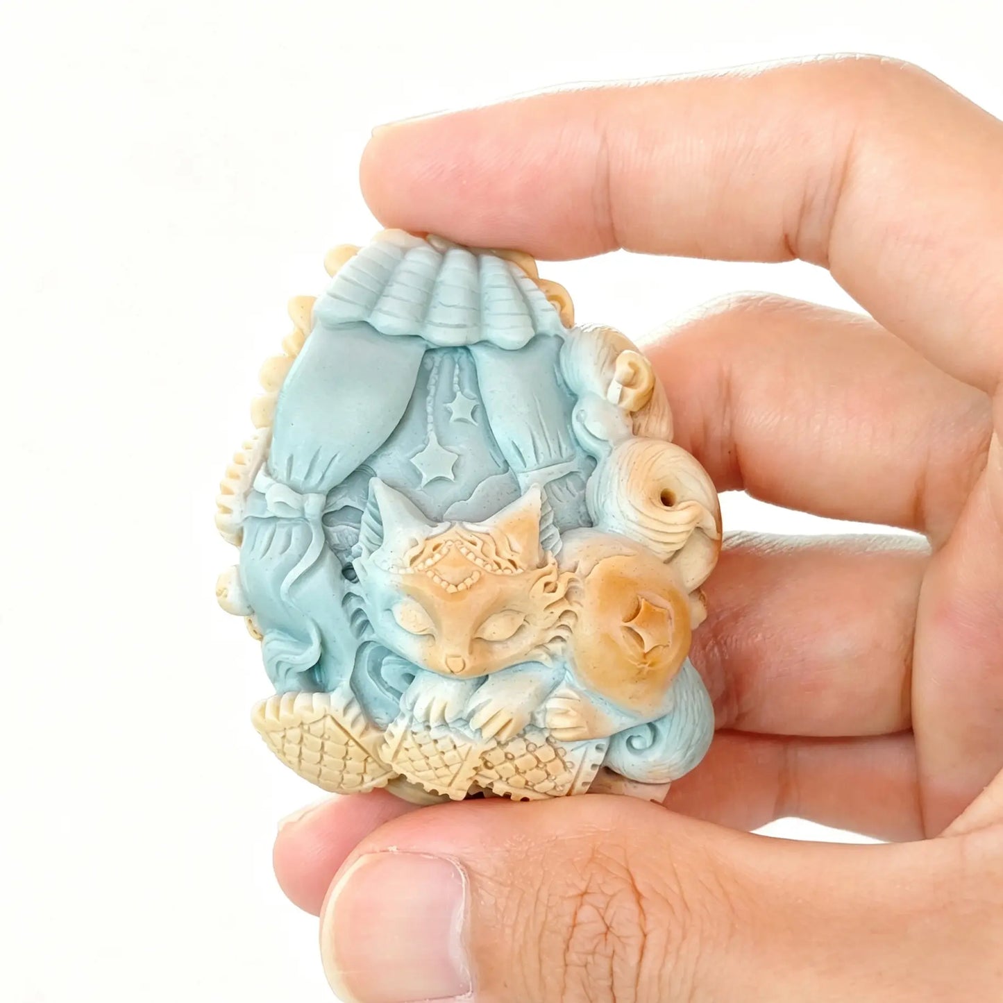 Handheld view of 4cm natural blue and honey yellow Alashan agate carved sleeping fox resting under a canopy bed with star details