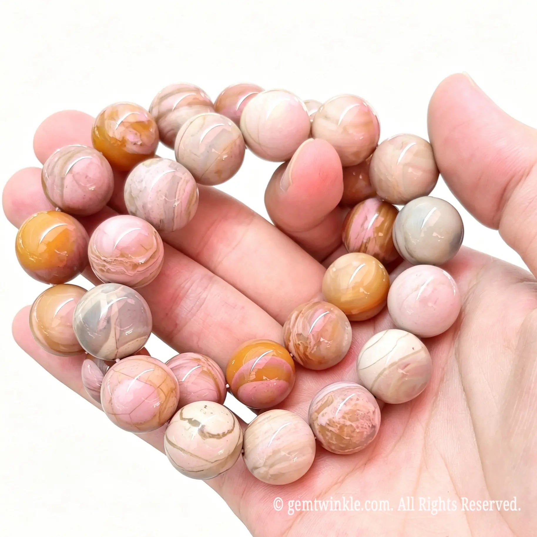 Handheld angle view of stacked Alashan crackle agate round bead stretch bracelets showcasing soft terracotta and pink tones