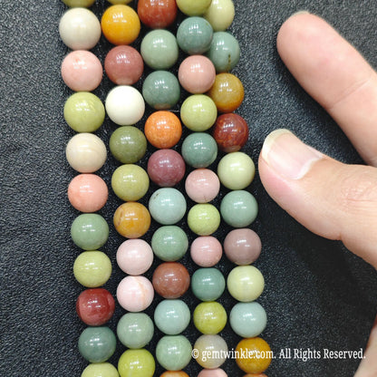 Finger pointing to natural multicolor Alashan Gobi agate round beads on strands for size reference and inspection