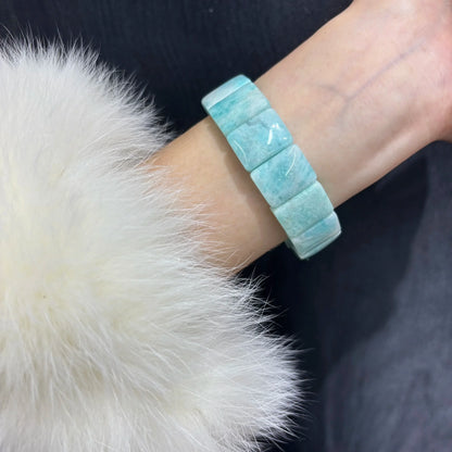Woman wearing the Amazonite Square Bead Bangle on her wrist, styled with a white fur accessory for a chic look.